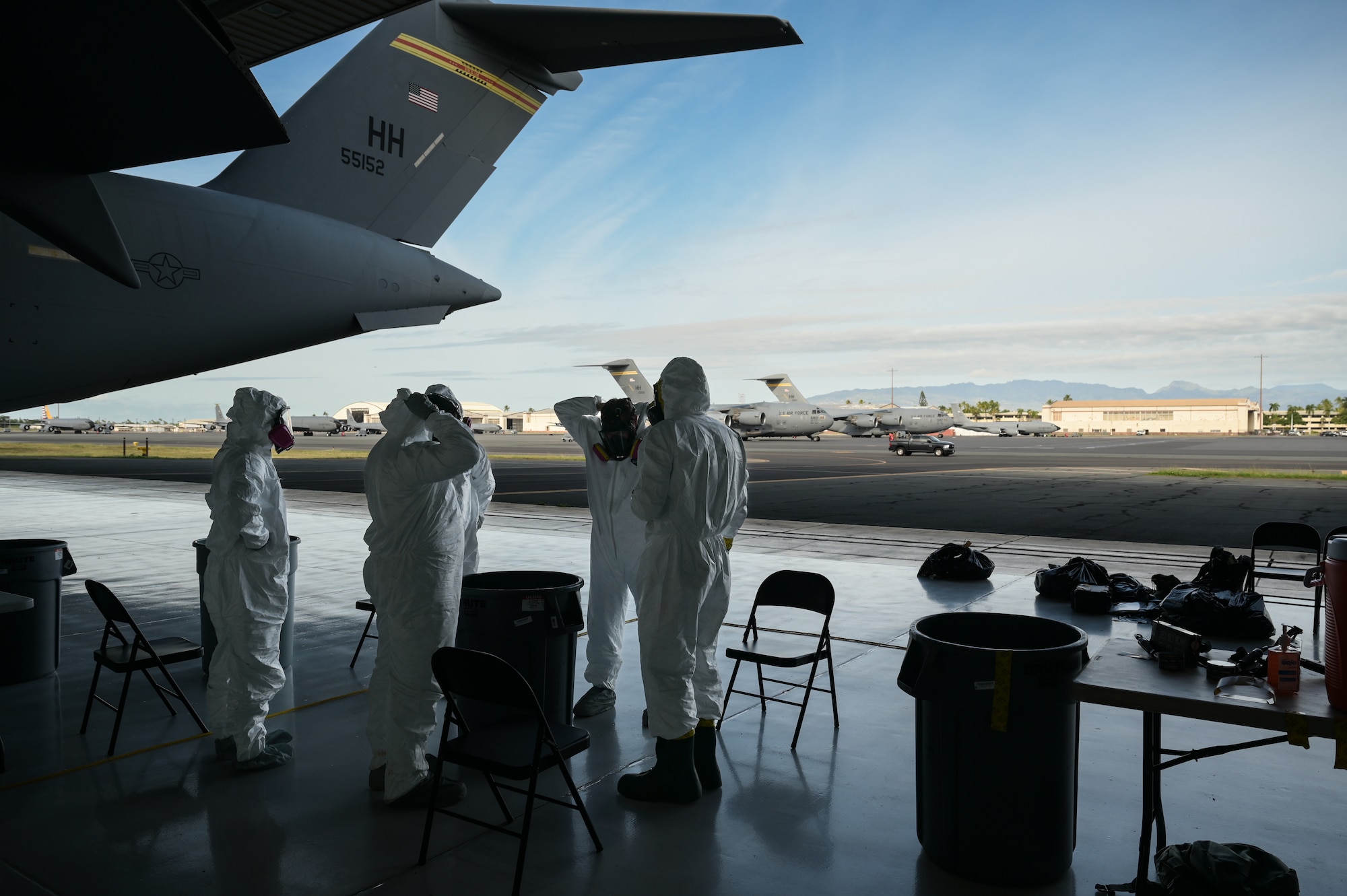 A group of Airmen dressed in equipment protection gear stand inside of an aircraft hangar.