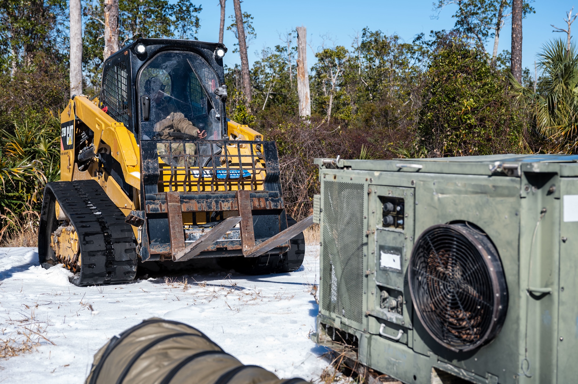 A U.S. Airman assigned to the 11th Air Task Force prepares to use a compact track loader vehicle to remove a faulty heating, ventilation and air conditioning unit at Tyndall Air Force Base, Florida, Jan. 22, 2025. Civil engineer Airmen worked to repair and replace faulty HVAC units during a winter freeze. (U.S. Air Force photo by Senior Airman Jasmyne Bridgers-Matos)