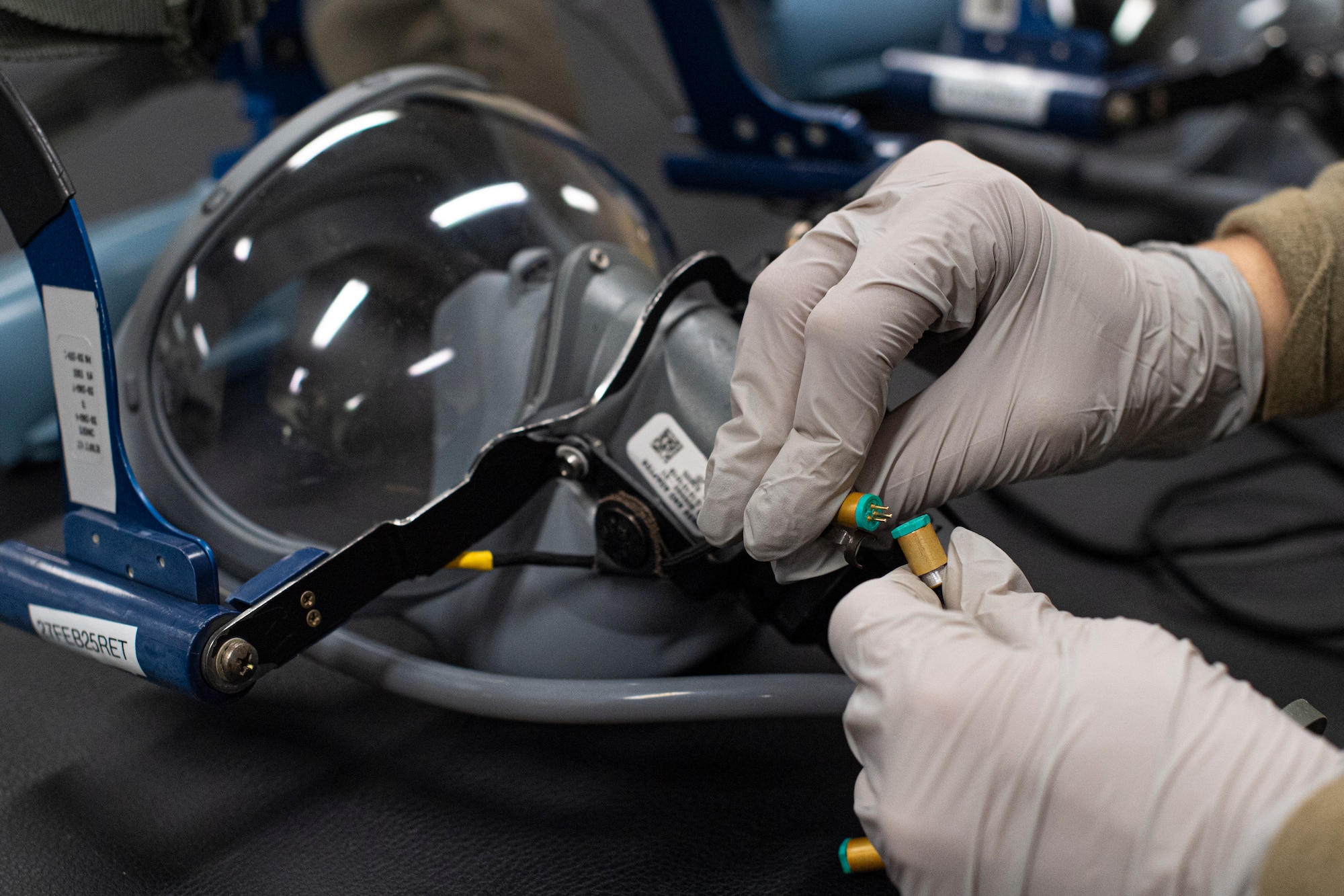 An Airman connects a microphone cable on a folding quick don mask.
