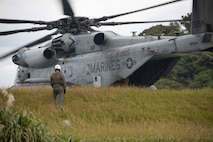 A U.S. Marine with SQUADRON watches a CH-53E Super Stallion during Helicopter Support Team training at Landing Zone Swan, Okinawa, Japan, Dec. 9, 2024. HST are operations conducted to train landing support specialists and pilots to transfer heavy equipment and supplies utilizing helicopters. (U.S. Marine Corps photo by Lance Cpl. Marcus Henson)