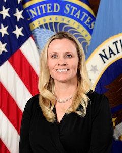 Official portrait of a woman standing in front of flags.