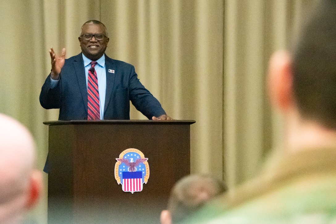 A man stands on stage behind a lectern speaking to a group of people.