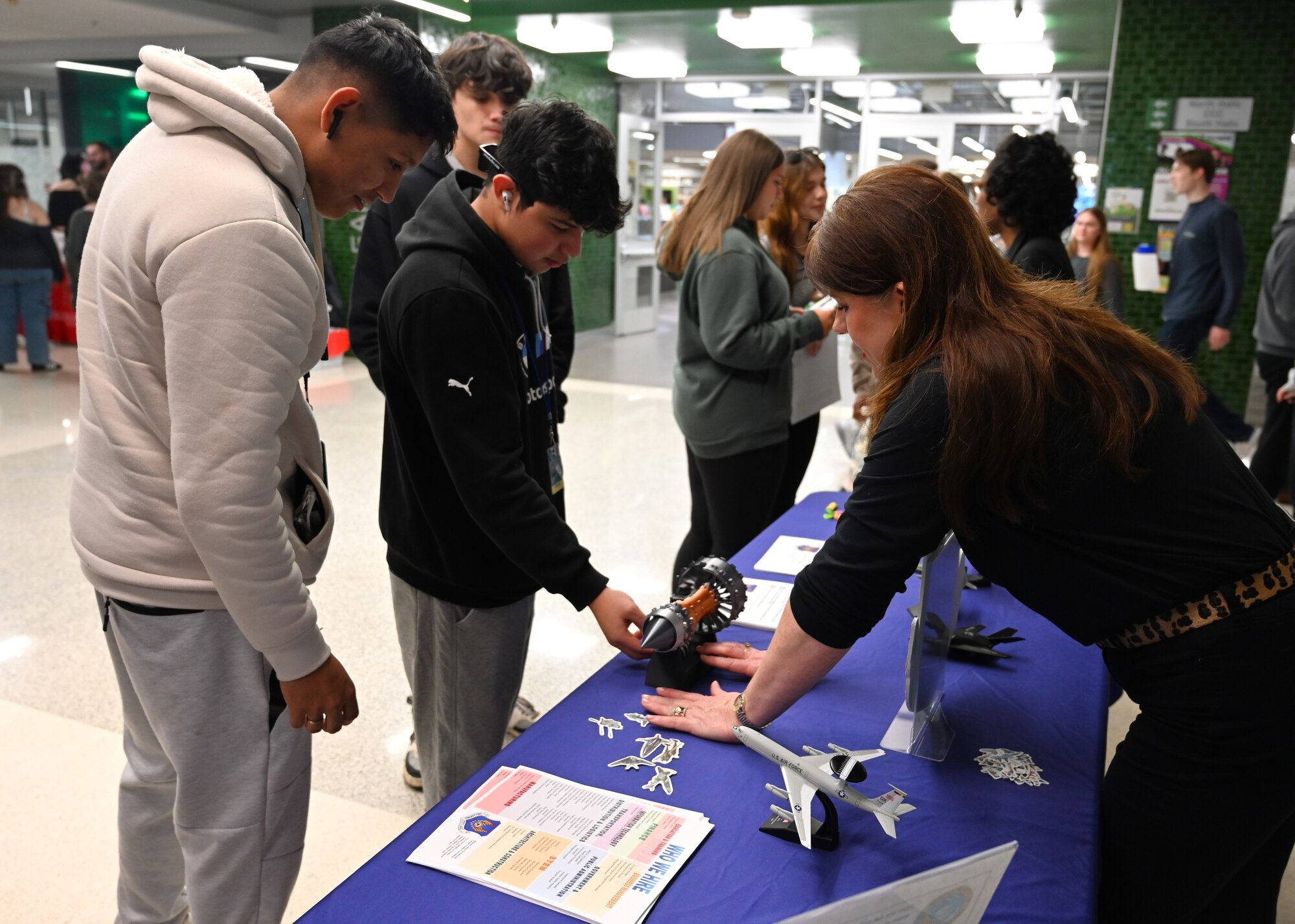 Students looking at a static of tiny aircrafts and an engine displayed on a table