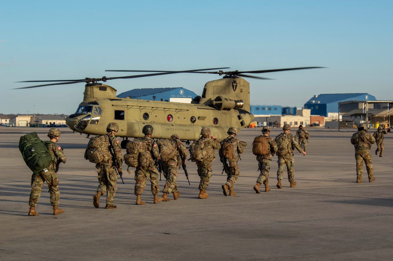 People in uniform and wearing backpacks walk toward a helicopter.