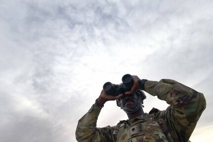 A soldier looks through binoculars.