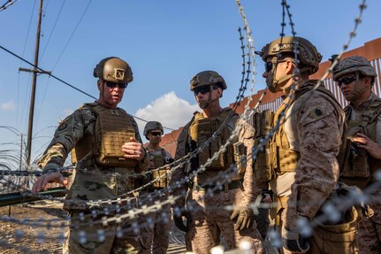 Five military personnel work together to install wire fencing.