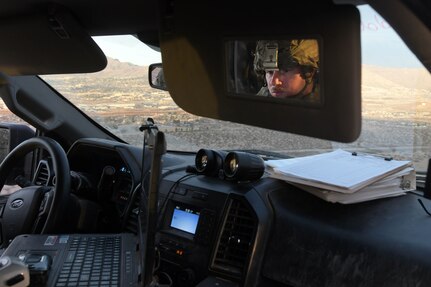 A soldier is reflected through a rearview mirror of a military vehicle.