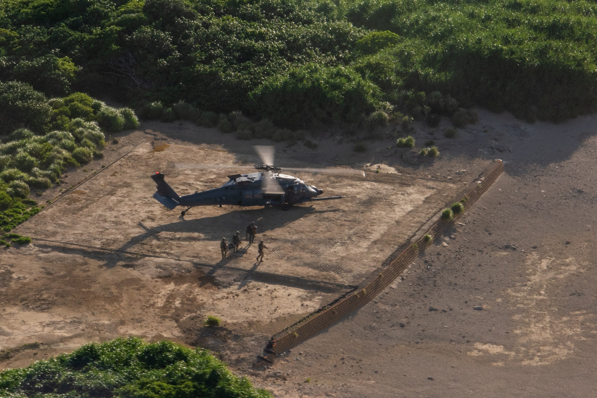 birds eye view of military members carrying a stretcher towards a helicopter
