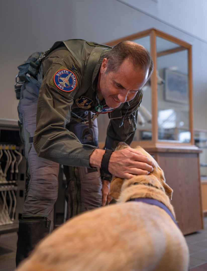 Captain, facility therapy dog, 114th Fighter Wing, greets Col. Jon Friedman, deputy commander, 114th Fighter Wing, as he prepares to fly June 24, 2025, at Joe Foss Field, South Dakota.