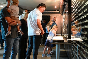 Men, women and children in summer casual clothes look at the guestbooks and inscriptions on a memorial wall.