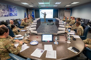 Air Force members watch man give presentation at big screen. Everyone is wearing fatigues.