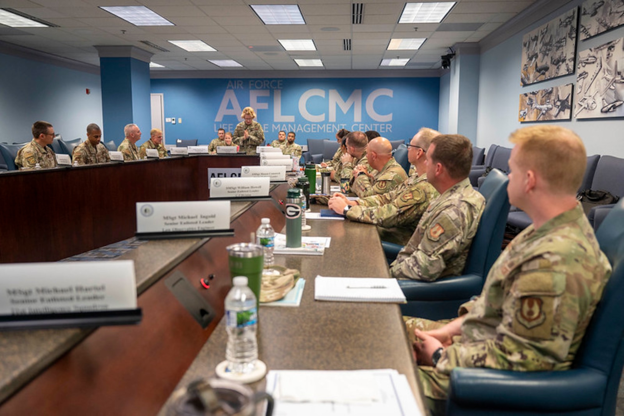 Air Force members sit around long table while wearing fatigues.