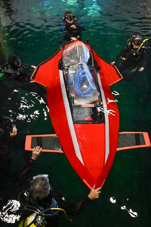Support divers guide Javelin 2.0 into position at the start of a race. The carbon fiber and foam core vessel were built in the Barone family’s garage and piloted by 16-year-old Quinn Barone. Carderock, the Navy's ship design and innovation powerhouse, provides the technical foundation for the future fleet through world-class research, development, and testing. (U.S. Navy photo by Devin Pisner)