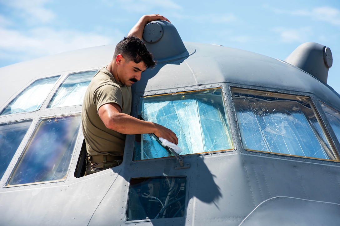 A close-up of an airman washing the windshield of an aircraft against a blue sky.