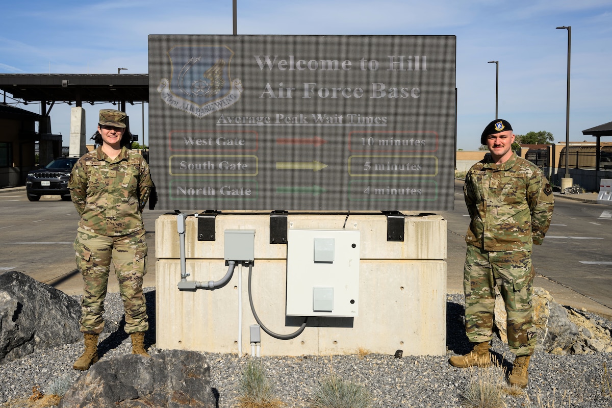 Senior Airman Jenna Skinner (left), 75th Communications and Information Directorate, and Tech. Sgt. Kyle Williamson, 75th Security Forces Squadron, stand next to the West Gate marquee which displays wait times at each of Hill's access points. The information is a result of an innovative project that captures data from the Utah Department of Transportation. (U.S. Air Force photo by R. Nial Bradshaw)