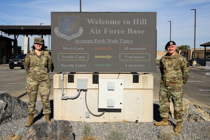 Senior Airman Jenna Skinner (left), 75th Communications and Information Directorate, and Tech. Sgt. Kyle Williamson, 75th Security Forces Squadron, stand next to the West Gate marquee which displays wait times at each of Hill's access points. The information is a result of an innovative project that captures data from the Utah Department of Transportation. (U.S. Air Force photo by R. Nial Bradshaw)