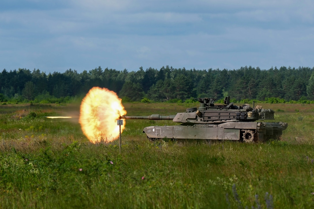 Soldiers fire a tank in a field creating a large fireball.