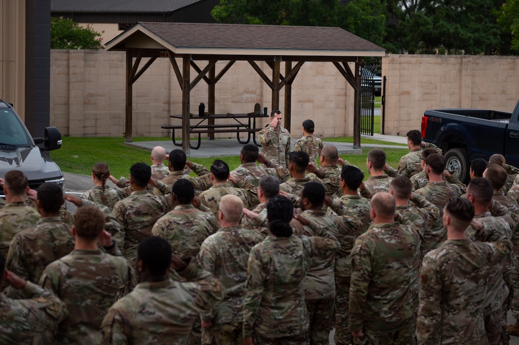 A group of people dressed in United States Air Force uniform salute a man who is saluting back.