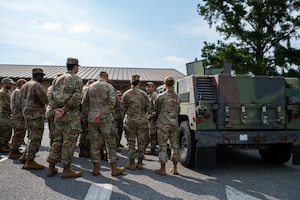 A group of people dressed in United States Air Force uniform are standing by a vehicle as a man instructs.