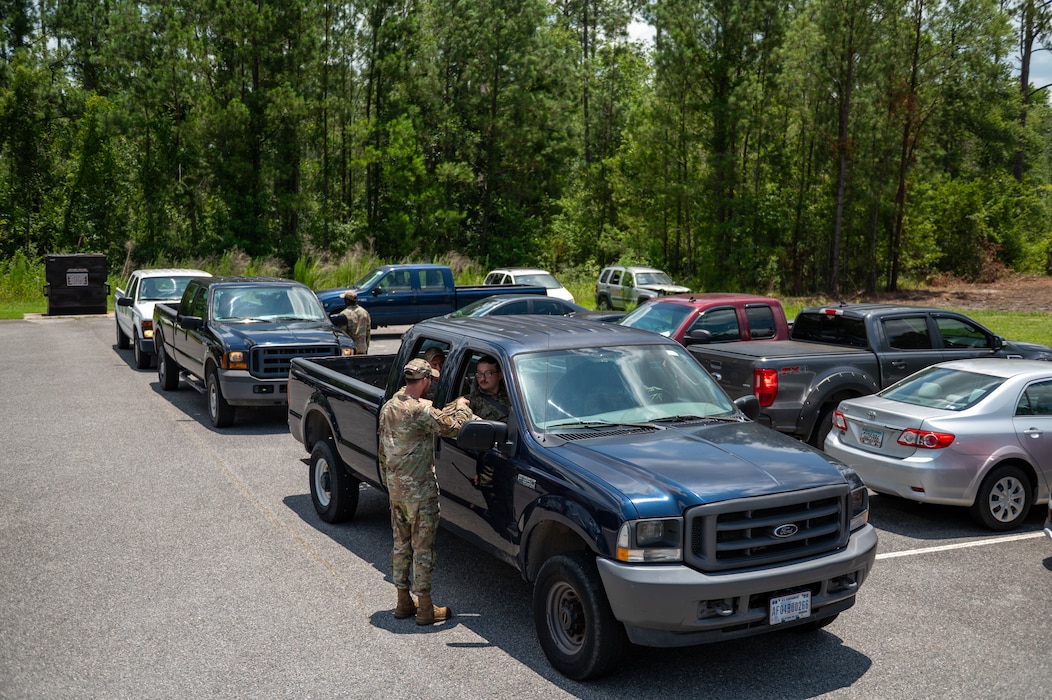 Man stands next to a trucks with it's window down, talking to the passenger. A line of trucks follow behind the truck.