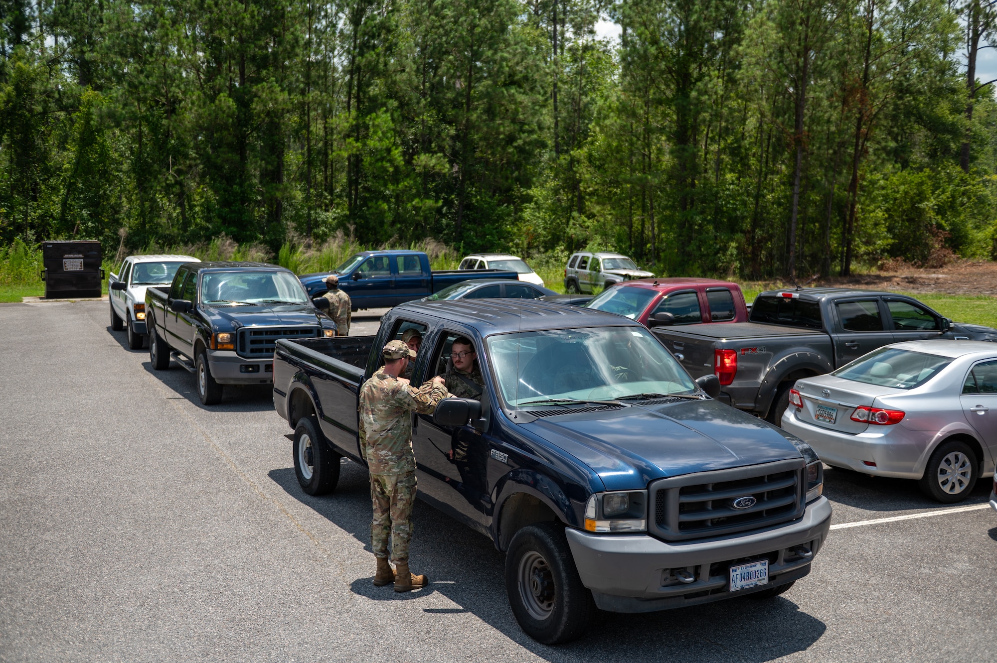 Man stands next to a trucks with it's window down, talking to the passenger. A line of trucks follow behind the truck.