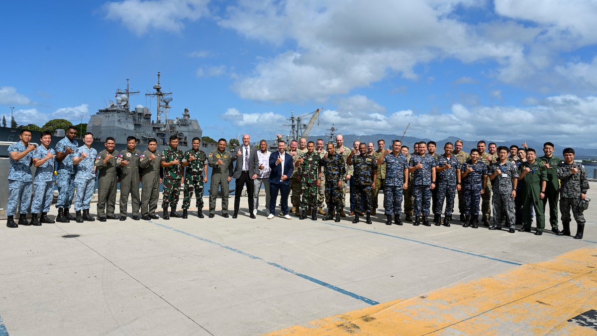 A line of people in front of 3 warships at dock
