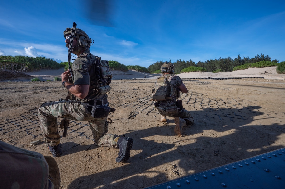 military members lean on the ground outside of a helicopter