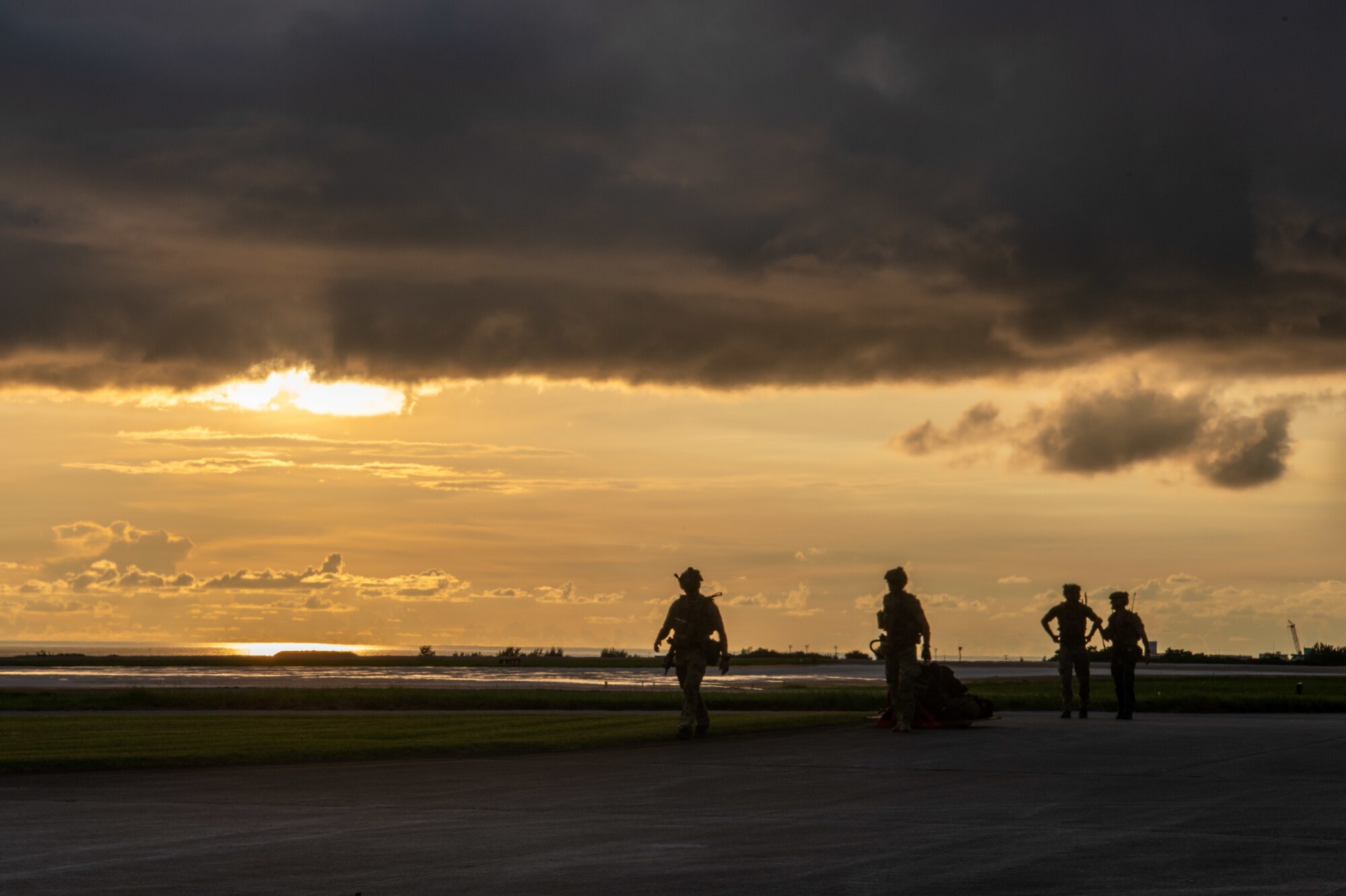 military members walk on the flightline silhouetted during the sunset