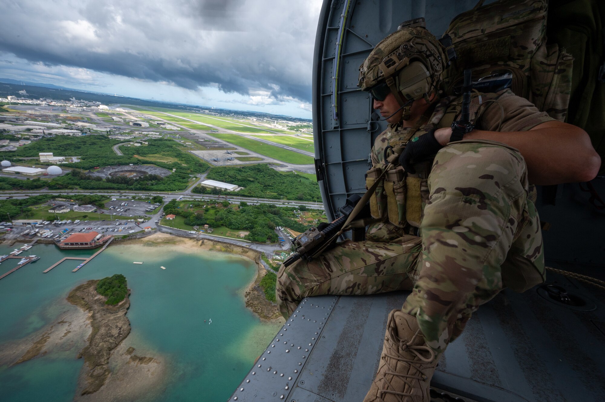 military member sits on a helicopter overlooking the coast of Okinawa