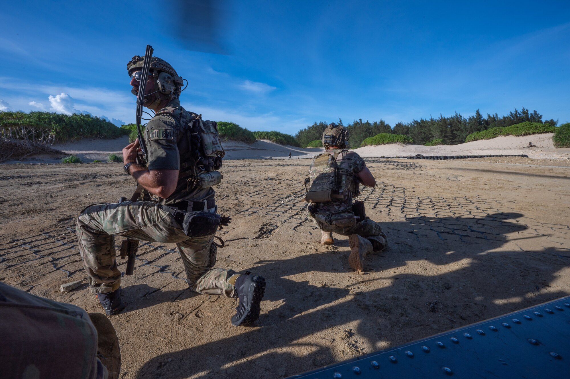 military members lean on the ground outside of a helicopter