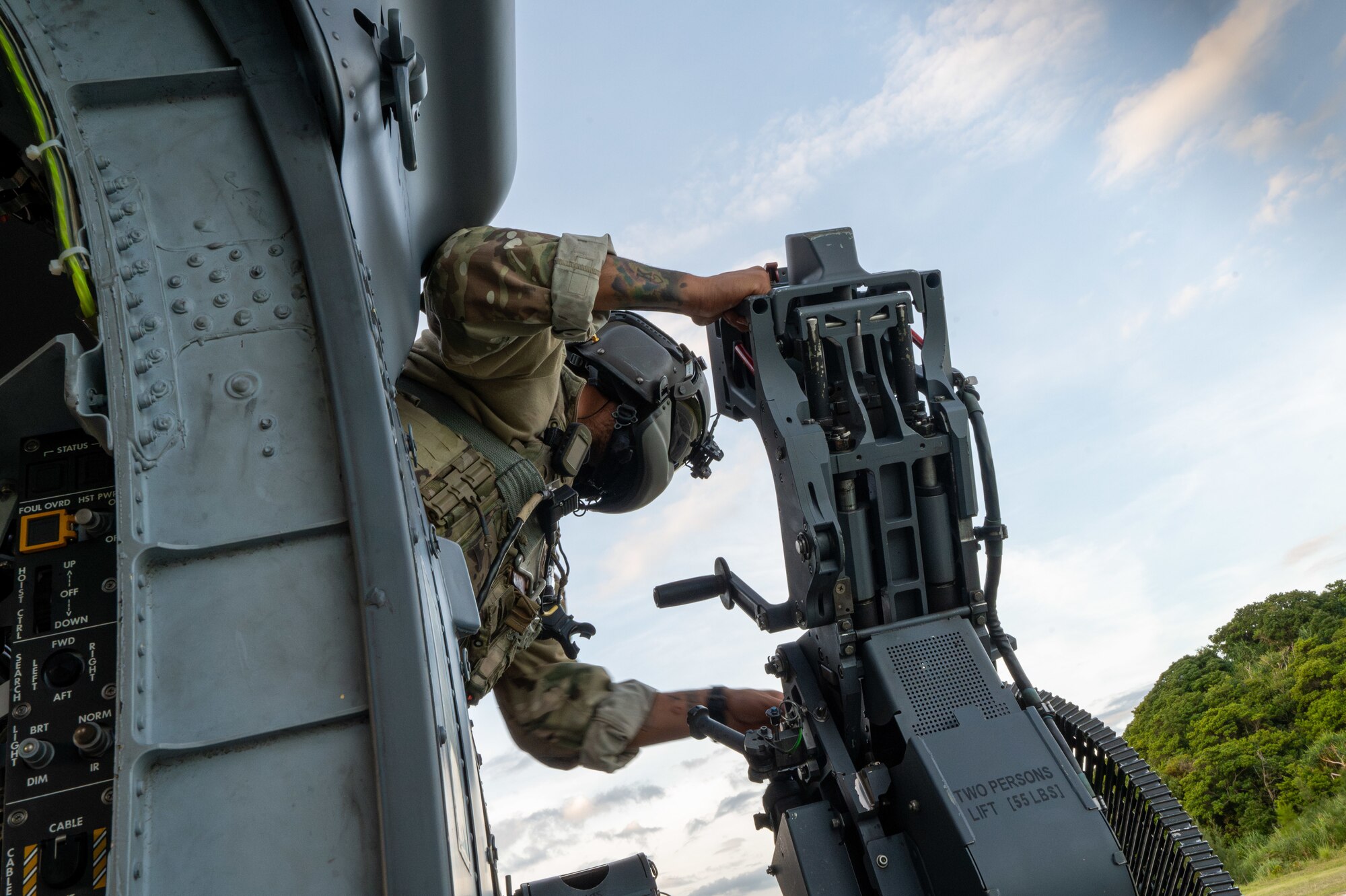 military member leans out of a helicoper window to work on the machine gun