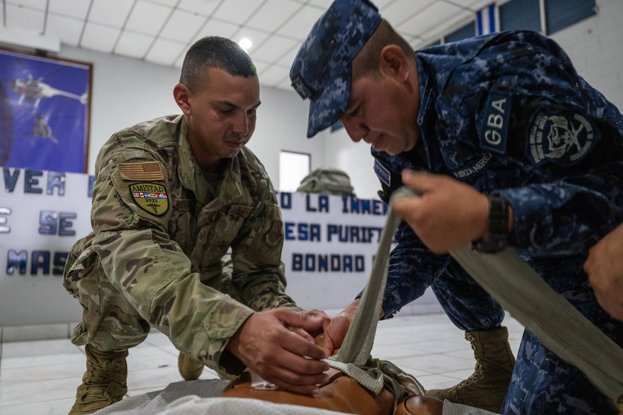 A man in U.S. Air Force uniform and a second man in El Salvador Air Force uniform apply a medical bandage.