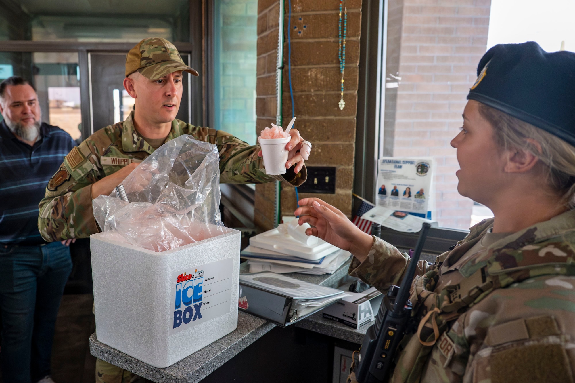 U.S. Air Force Senior Master Sgt. Keith Whipple, first sergeant from the 355th Security Forces Squadron, hands shaved ice to an Airman at Davis-Monthan Air Force Base, Arizona, July 1, 2025. The Military Affairs Committee and base first sergeants aimed to boost morale and show appreciation for Airmen enduring high temperatures on the flight line and in other outdoor areas by handing out shaved ice. (U.S. Air Force photo by Airman Samantha Melecio)