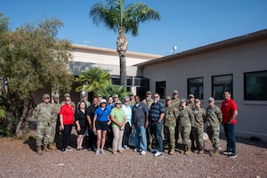 U.S. Air Force Airmen and Military Affairs Committee members pose for a group photo in front of the community center at Davis-Monthan Air Force Base, Arizona, July 1, 2025. The MAC partnered with the First Sergeants Council to visit various squadrons and hand out shaved ice, offering a refreshing break from the heat while fostering connection and morale among Airmen. (U.S. Air Force photo by Airman Samantha Melecio)