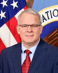 Photo of a man in a suit standing in front of flags.