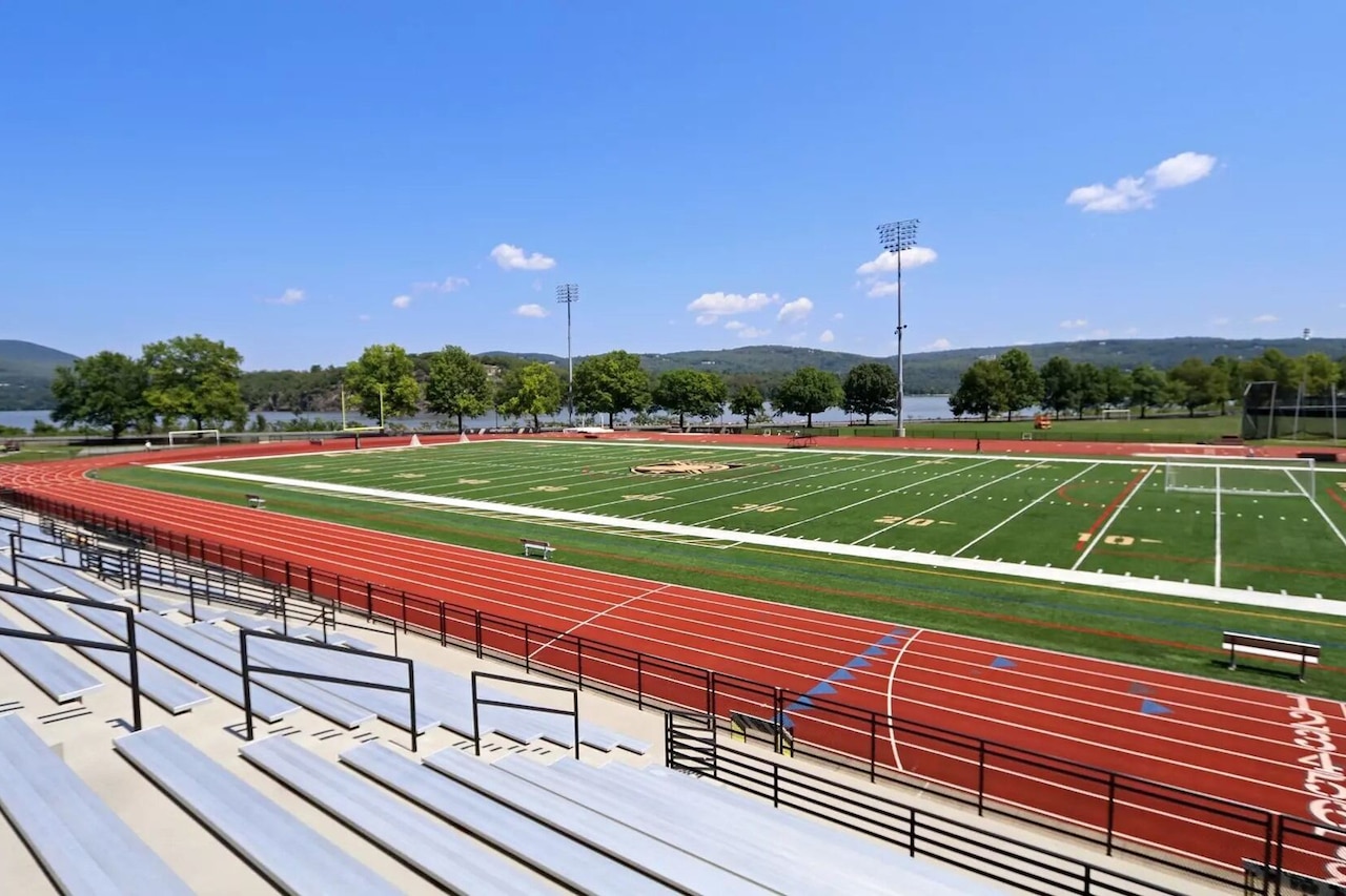 A lined track surrounds a grassy field. Bleachers stand in the background.