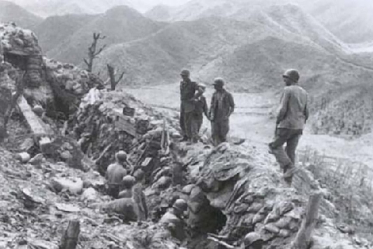 Soldiers stand in a deep trench while others stand above them, looking down.