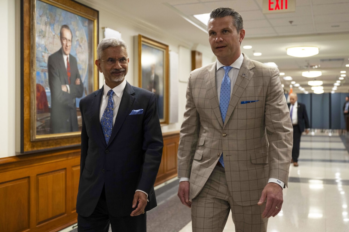 Two men wearing suits walk down a hallway together. Large portraits adorn the walls.