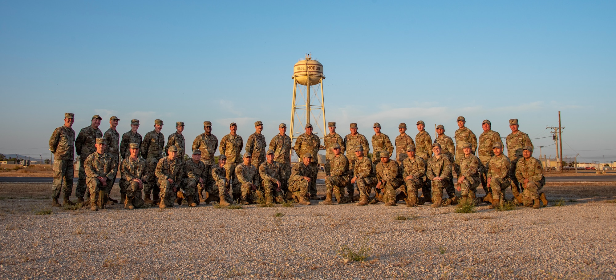 a group photo of 134th ARW civil engineers at sunrise with the Moron Air Base water tower behind them.