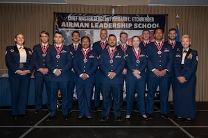 A group of students and their two supervisors stand on a stage for a group photo.