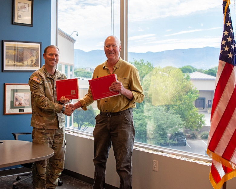 Lt. Col. Matthew Miller, left, commander, USACE-Albuquerque District, and Armand Groffman, vice president of the Regina, N.M., Mutual Domestic Water Consumers Association, shake hands while holding up the environmental infrastructure agreement they just signed at the Albuquerque District’s headquarters, June 27, 2025.