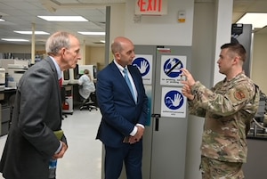Two men in suits listen to a man in military uniform speaking.