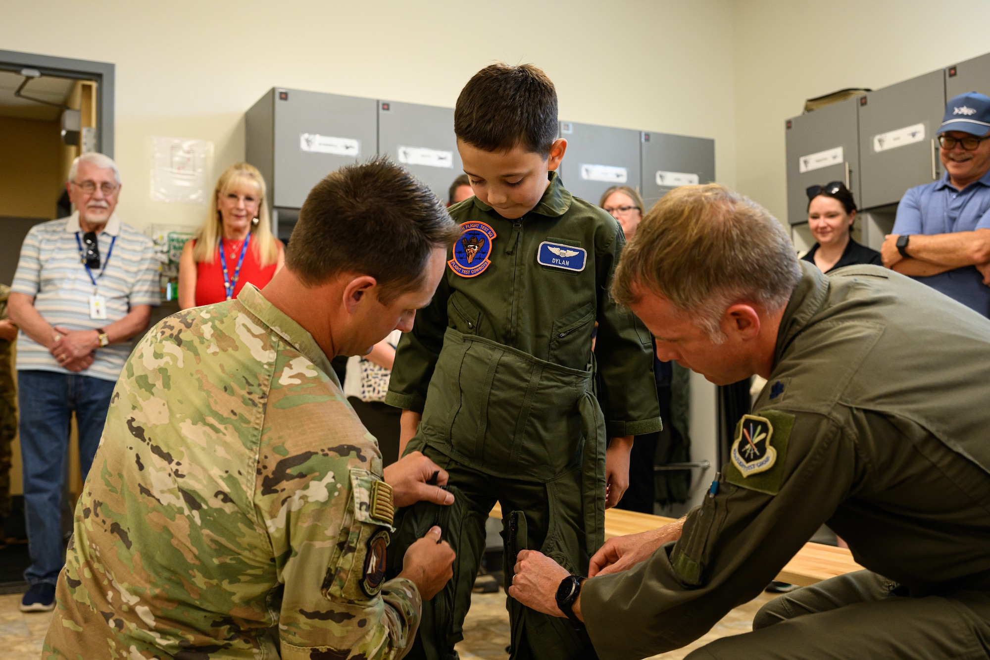 An aircrew member and pilot help Dylan zip up a G-suit.