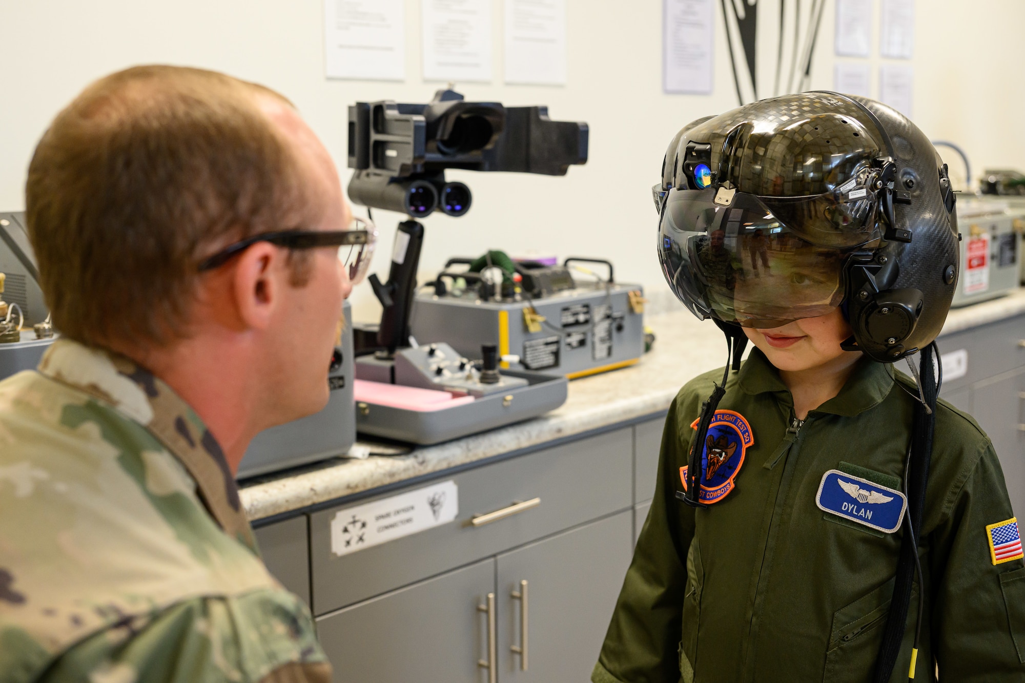 Dylan wearing a pilot helmet while an aircrew member kneels down looking at him in the foreground.