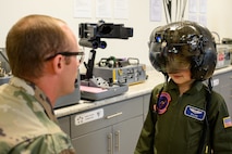 Dylan wearing a pilot helmet while an aircrew member kneels down looking at him in the foreground.