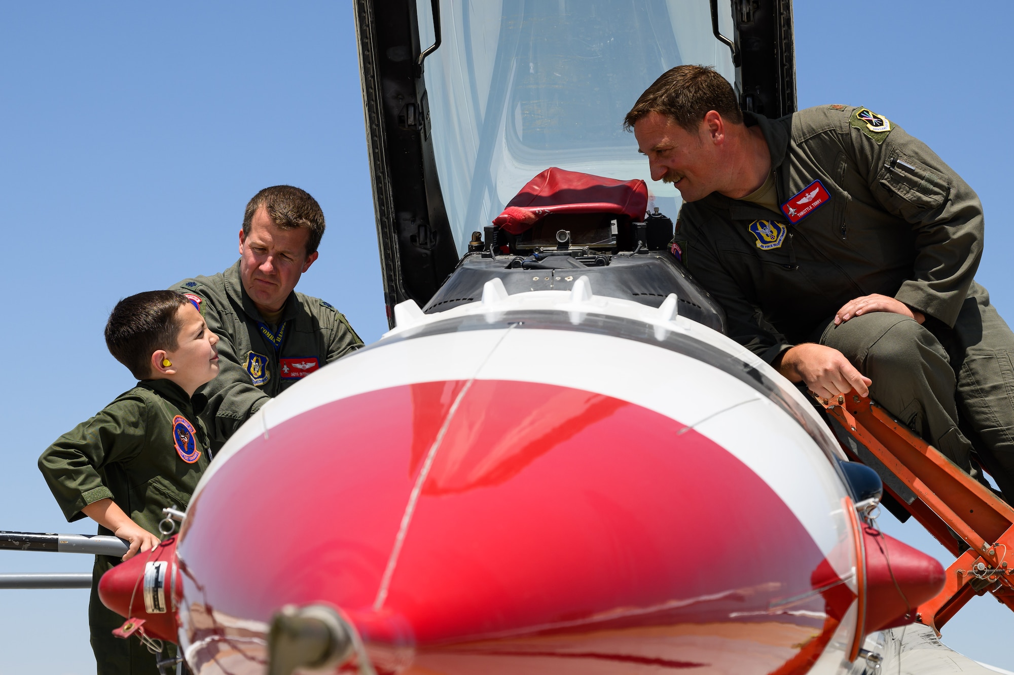 Dylan and two pilots standing on ladders peak into the cockpit of an F-16.