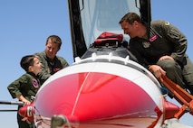 Dylan and two pilots standing on ladders peak into the cockpit of an F-16.
