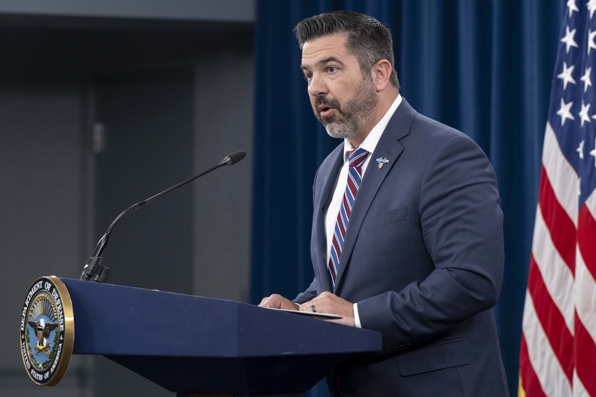 A man in business attire stands behind a podium, speaking into a microphone.