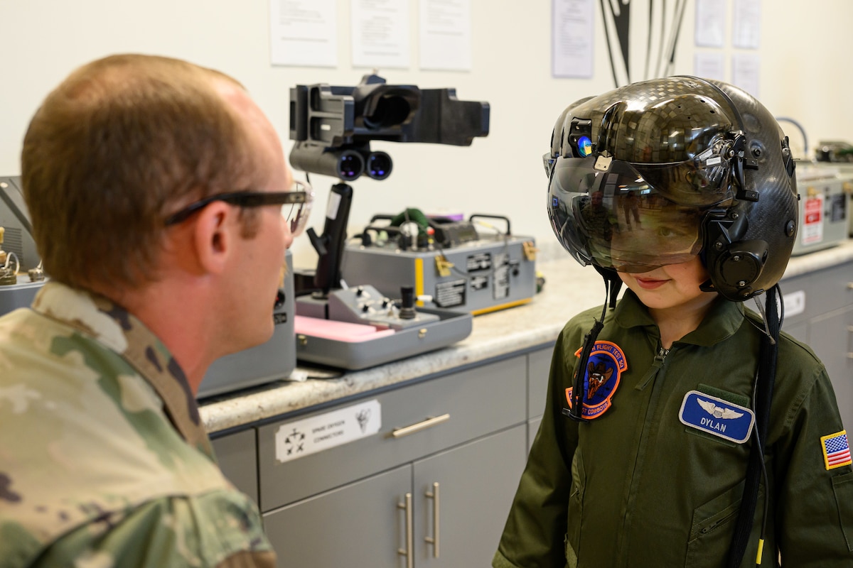 Dylan wearing a pilot helmet while an aircrew member kneels down looking at him in the foreground.