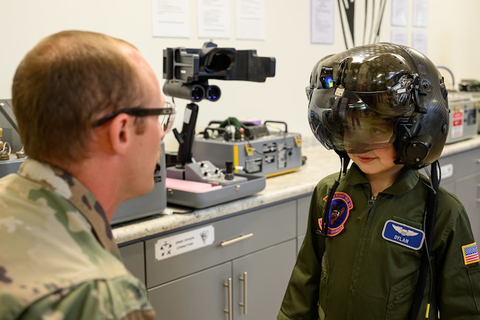 Dylan wearing a pilot helmet while an aircrew member kneels down looking at him in the foreground.